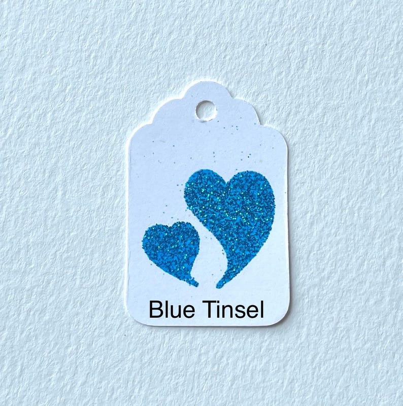 May include: A white gift tag with a blue glitter heart design. The tag says "Blue Tinsel" at the bottom.