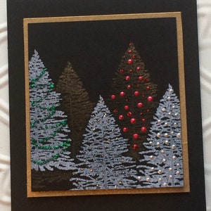 May include: A Christmas card with a black background and a gold border. The card depicts a forest of stylized evergreen trees in shades of grey, brown, and white, some decorated with red and green embellishments. The design creates a festive winter scene.