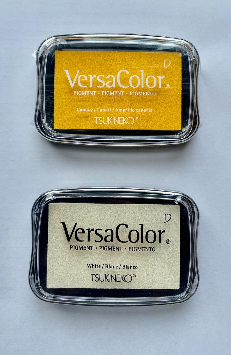 May include: Two ink pads, one yellow and one white, with the text "VersaColor" and "TSUKINEKO" on them. The ink pads are in clear plastic cases.