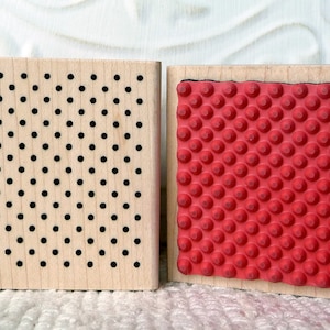 May include: Two wooden blocks with different patterns. The block on the left has a black dot pattern. The block on the right has a red rubber surface with a raised dot pattern.