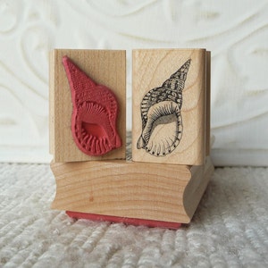Op de afbeelding: Twee houten rubberen stempels met een schelpontwerp. Een stempel is rood en de andere is zwart-wit.