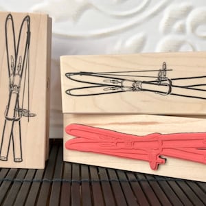 May include: Three wooden blocks with different images of skis. The top block has a black and white image of skis with bindings. The middle block has a black and white image of skis with bindings. The bottom block has a red image of skis with bindings.