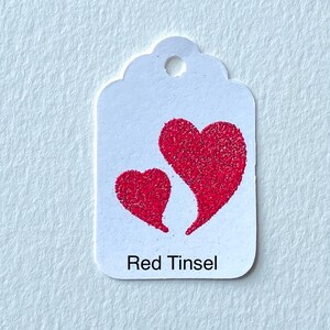 May include: White gift tag with two red glitter hearts and the text "Red Tinsel".