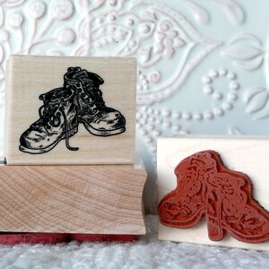 May include: Two wooden rubber stamps with images of boots. The first stamp features a pair of black and white boots with laces. The second stamp features a pair of red boots with a floral design.