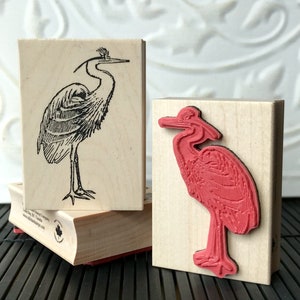 May include: Two wooden blocks with a black and white line drawing of a heron on one block and a red rubber stamp of a heron on the other block.