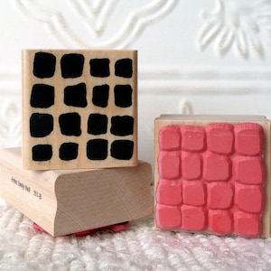 Könnte beinhalten: Drei Holzstempel mit verschiedenen Mustern. Der obere Stempel hat ein schwarz-weißes geometrisches Muster. Der mittlere Stempel ist leer. Der untere Stempel hat ein rotes Ziegelmuster. Der untere Stempel ist mit "Annie Emily Hall 501B" beschriftet.