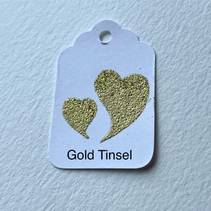 May include: White gift tag with two gold glitter hearts and the text "Gold Tinsel".