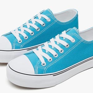 May include: A pair of bright turquoise low-top sneakers featuring white laces, white rubber toe caps, and thick white soles with a thin black stripe detail. The canvas upper is a solid, vibrant blue color with silver-toned metal eyelets.