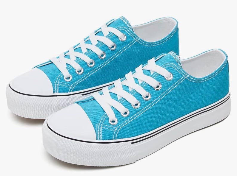 May include: A pair of bright turquoise low-top sneakers featuring white laces, white rubber toe caps, and thick white soles with a thin black stripe detail. The canvas upper is a solid, vibrant blue color with silver-toned metal eyelets.