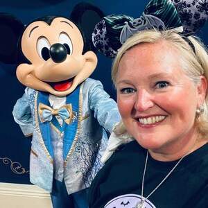 May include: A Mickey Mouse character figure wearing a light blue and gold tuxedo with a matching bow tie, standing next to a person wearing a black headband with two ears featuring a green and black striped pattern, a bat graphic, and a black lace overlay.