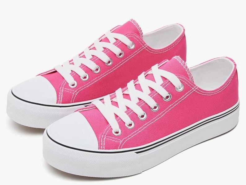 May include: A pair of low-top canvas sneakers in a vibrant hot pink color. The shoes feature white laces, white rubber toe caps, and thick white rubber soles with a thin black stripe detail running along the side of the platform base.