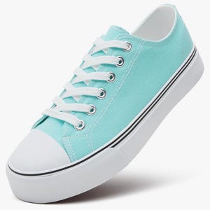 May include: A low-top sneaker in a bright turquoise color featuring a white rubber toe cap, white laces, and silver-toned metal eyelets. The shoe has a thick white rubber sole with two thin black horizontal stripes running along the side.