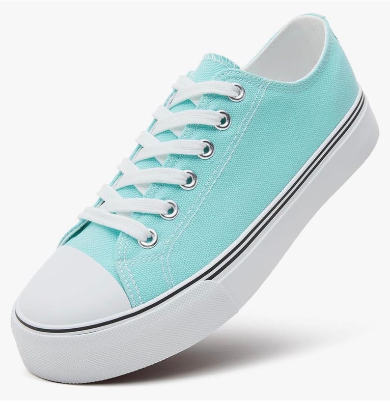 May include: A low-top sneaker in a bright turquoise color featuring a white rubber toe cap, white laces, and silver-toned metal eyelets. The shoe has a thick white rubber sole with two thin black horizontal stripes running along the side.