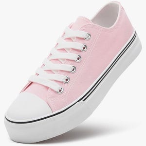 May include: A low-top sneaker featuring a light pink canvas upper, white laces, and silver-toned metal eyelets. The shoe includes a white rubber toe cap and a thick white rubber sole accented with two thin black horizontal stripes along the side.