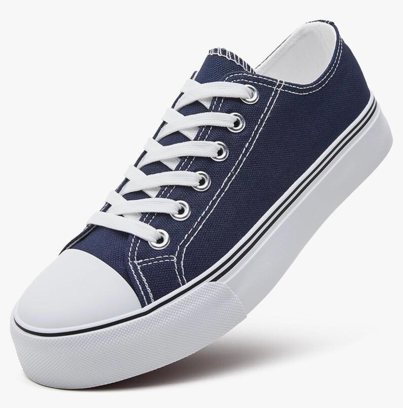 May include: A low-top sneaker featuring a dark navy blue canvas upper, white laces, and silver-toned metal eyelets. The shoe includes a white rubber toe cap and a thick white platform sole with thin black horizontal stripes along the side.