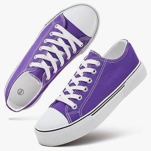 May include: A pair of purple canvas sneakers featuring white laces, white rubber toe caps, and thick white soles with thin black stripes. The interior of the shoe shows a size label with the numbers 6 and 37 printed on a white background.