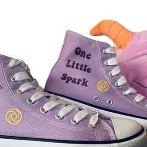 May include: Purple high-top canvas sneakers with a dragon and swirl designs on one shoe and the text "One Little Spark" on the other shoe.