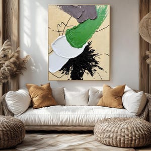 Pode incluir: Um sof&aacute; branco com almofadas marrons fica em frente a uma grande pintura abstrata com tinta verde, preta, branca e roxa. A pintura est&aacute; em uma parede bege. O sof&aacute; est&aacute; em uma sala com piso de madeira e uma l&acirc;mpada de vime pendurada no teto.