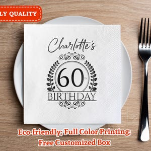 Può includere: Un tovagliolo quadrato bianco con la scritta "Charlotte's 60th Birthday" in nero, posto su un piatto bianco. A destra c'è una forchetta nera. Il tovagliolo ha un motivo a ghirlanda decorativa attorno al numero 60. Le parole "3-PLY QUALITY" sono in un riquadro rosso.