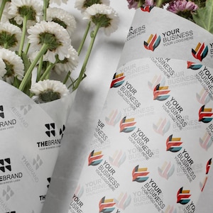 Puede incluir: Flores blancas envueltas en papel de seda impreso personalizado. El papel presenta un patrón repetido de un logotipo colorido y el texto "YOUR BUSINESS YOUR LOGO HERE". El logotipo de la marca también está impreso.