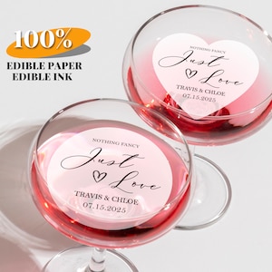 May include: Two wine glasses filled with pink liquid, each with a heart-shaped sticker that reads "Nothing Fancy Just Love" with a couple's names and a date. The image also includes text that says "100% Edible Paper Edible Ink."