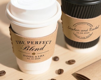 May include: Two coffee cups with brown sleeves. One cup is white with the text "THE PERFECT Blend" and "DANIEL & LISA 04.12.2026". The other cup is black with the text "THE PERFECT BLEND Stephen and Rachel 04.09.2026 SAVE THE DATE". Coffee beans are scattered around.