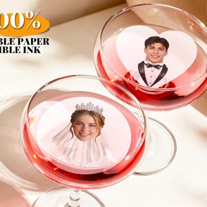 Puede incluir: Dos copas de cristal transparente con líquido rojo, cada una con un disco de papel comestible. Uno muestra a una persona con esmoquin dentro de un corazón, el otro a una persona con tiara y velo. Texto: 100% EDIBLE PAPER EDIBLE INK.
