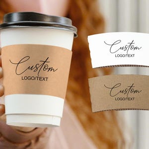 Puede incluir: Una taza de café de papel blanco con tapa negra y una funda de papel marrón. La funda tiene la palabra "Custom" en fuente cursiva, con "LOGO/TEXT" debajo. Se muestran dos fundas adicionales, una blanca y otra marrón.