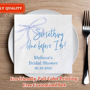 Puede incluir: Una servilleta cuadrada blanca con el texto "Something blue before I do!" en azul, con una ilustración de un lazo azul. La servilleta está sobre un plato blanco, junto a un tenedor plateado. El texto "Melissa's Bridal Shower 06.28.2026" también está impreso en la servilleta.