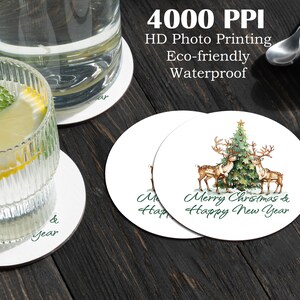 Puede incluir: Posavasos redondos blancos con un diseño de acuarela de un árbol de Navidad y renos, con el texto "Merry Christmas & Happy New Year". Los posavasos son impermeables y ecológicos.