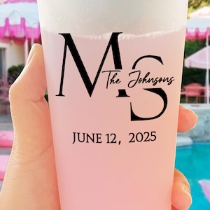 Puede incluir: Un vaso de plástico rosa con una capa de espuma blanca en la parte superior. El vaso tiene texto negro que dice "Ms The Johnsons" y "JUNE 12, 2025". El vaso está sostenido por una mano, con una piscina y sombrillas rosas en el fondo.