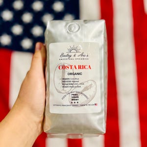 Może przedstawiać: Srebrna torba z organiczną kawą z Kostaryki. Etykieta głosi "Bailey & Ana's Ancestral Organics" i zawiera szczegóły dotyczące regionu, procesu, wysokości i palenia. Widoczny jest również tekst "Food the way God intended, feel your best".