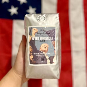 May include: A bag of coffee beans with a label that says "Bailey & Anas Ancestral Organics Never Surrender Blend" and features a picture of Donald Trump with the text "Fight, Fight, Fight!" and "Feel Your Best".