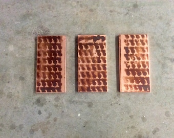 May include: Three rectangular copper plates arranged side by side, each featuring a repeating pattern of dark, semi-circular etched marks across the metallic surface. The copper has a warm, reddish-brown tone with visible variations in the finish.