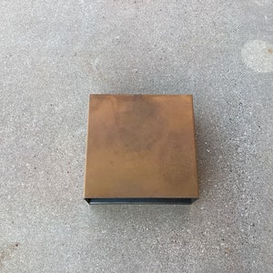 May include: A square, rusty brown metal wall sconce with a black trim around the edges.