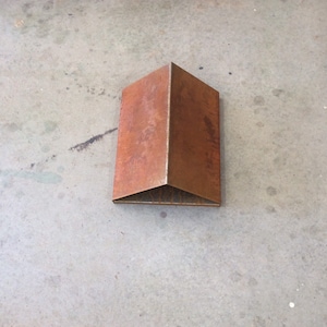 May include: A rusty metal sculpture in the shape of a house. The sculpture is sitting on a concrete surface.