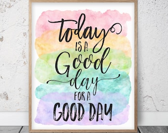 May include: A framed print with the words "Today is a Good Day for a Good Day" in black script. The background features watercolor washes in shades of pink, yellow, green, blue, and purple. The frame is a light brown color.