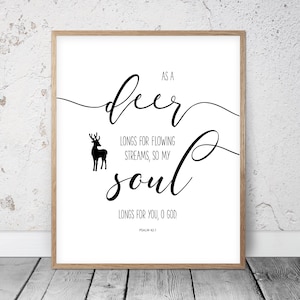 May include: A framed print with a white background and black script. The text reads "As a deer longs for flowing streams, so my soul longs for you, O God." A black silhouette of a deer is on the left. Psalm 42:1 is at the bottom.