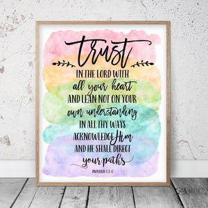 Puede incluir: Una impresión enmarcada con la palabra "trust" en escritura elegante sobre una cita de Proverbios 3:5-6. El fondo presenta lavados de acuarela en rosa, amarillo, verde, azul y morado. El texto es negro.