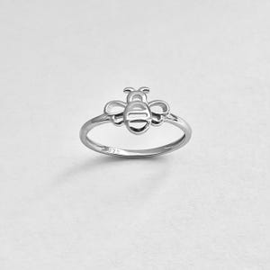 May include: A silver ring with a cutout bee design. The ring is marked with "925" on the inside band.