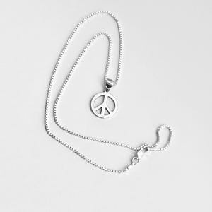 Könnte beinhalten: Eine silberne Halskette mit einem Friedenszeichen-Anhänger und einer Boxkette.
