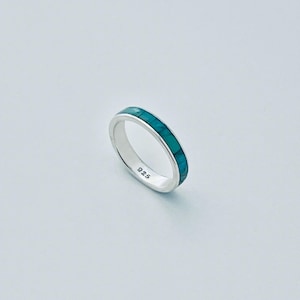 May include: A silver band ring featuring a continuous inlay of teal-colored stone segments around the exterior. The interior of the band is clearly stamped with the number 925, indicating the sterling silver composition of the jewelry piece.