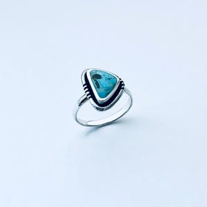 May include: A silver ring with a triangular turquoise stone set in a silver bezel. The stone has a blue and green color.