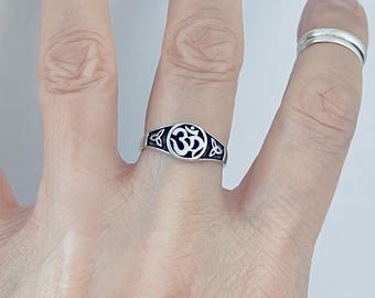 May include: A silver ring featuring a black and white Om symbol. The ring has a detailed design with Celtic knot accents. The ring is displayed on a finger, highlighting its size and style.