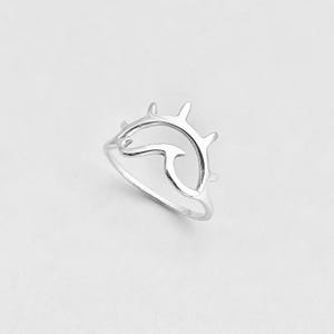 Könnte beinhalten: Ein silberner Ring mit einem Sonnen- und Wellenmotiv. Das offene Design des Rings zeigt eine stilisierte Sonne mit spitzen Strahlen über einer geschwungenen Welle. Der Ring besteht aus glänzendem, reflektierendem Metall und ist vor weißem Hintergrund.