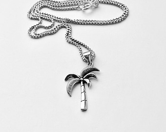 May include: A silver chain necklace with a palm tree pendant. The pendant is detailed with a textured trunk and leaves.