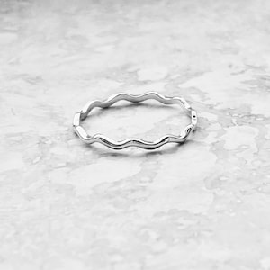 May include: A silver ring with a wavy design. The ring is simple and elegant.