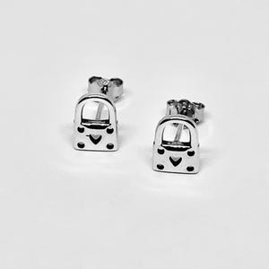 May include: A pair of silver stud earrings shaped like padlocks with a heart cutout in the center. The earrings have a small, silver post for insertion into the ear.