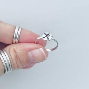 May include: A silver ring with a sand dollar design. The sand dollar has a small flower in the center.