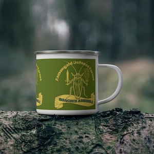 Può includere: Tazza smaltata bianca con grafica di scarafaggio giallo su sfondo verde. La tazza presenta il testo "Asmongold Defense Forces" e "Roaches Assemble". Ha un bordo argentato e un manico bianco.
